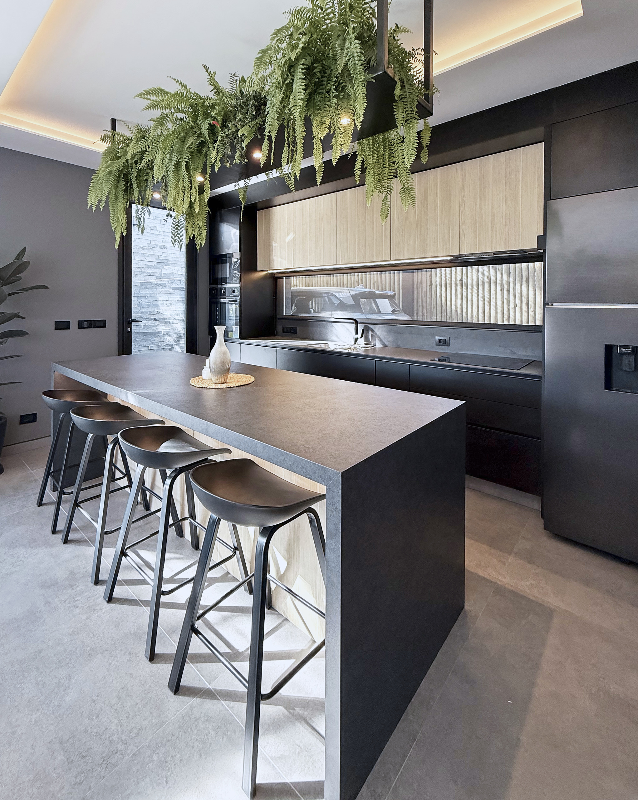Cocina con isla oscura, madera clara y vegetación suspendida