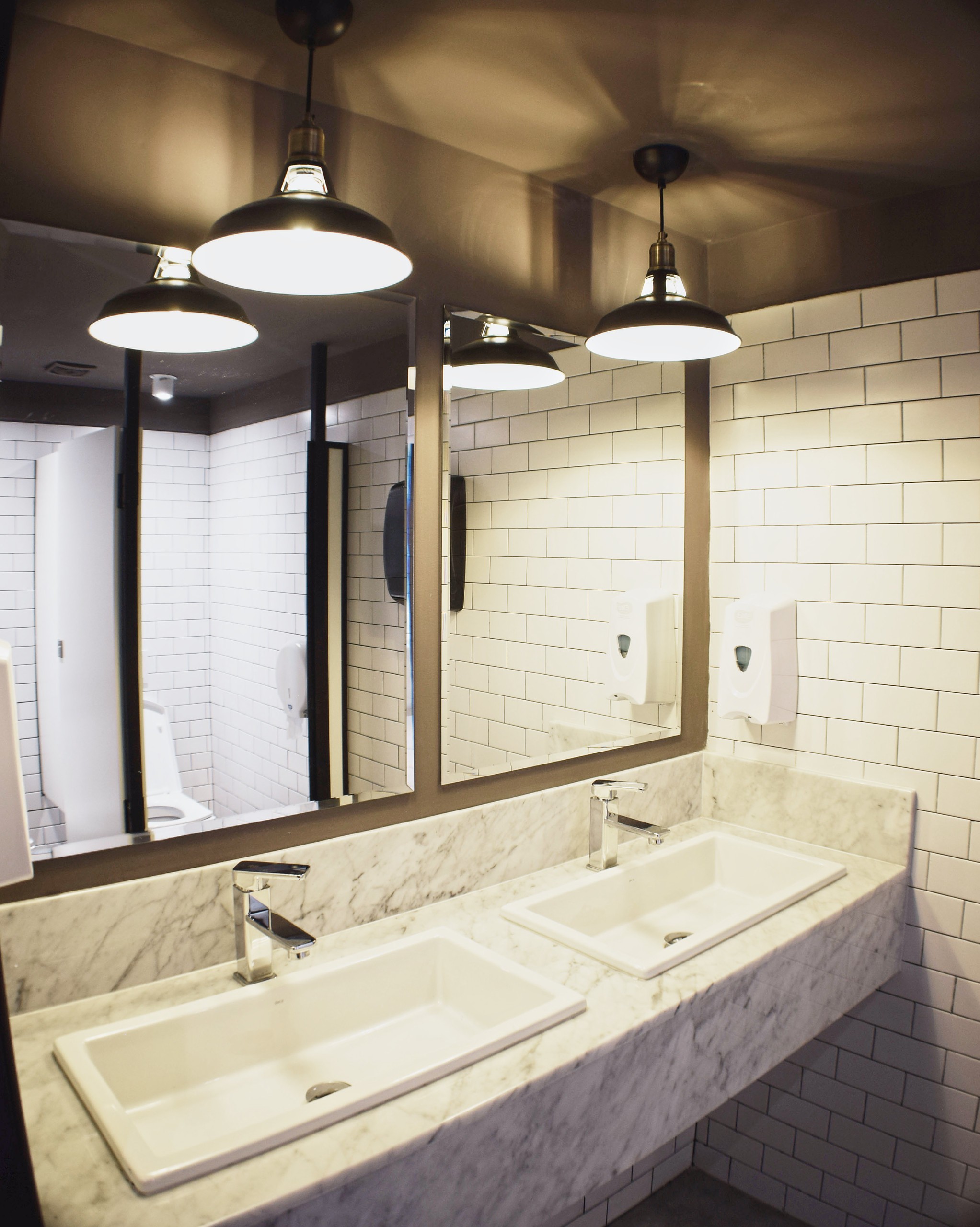 Baños de VIE Punta con mármol, azulejos blancos y luminarias colgantes